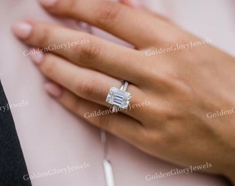 May include: A close-up of a hand wearing a silver ring with a large, clear, emerald-cut gemstone. The ring is set in a simple band and the gemstone is surrounded by smaller diamonds.