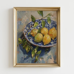 以下が含まれることがあります： 金色のフレームに入った油絵で、静物画を描いています。青と白の模様のボウルには、黄色と緑色のレモンがいくつか入っており、緑の葉と枝が付いています。鮮やかな構図です。