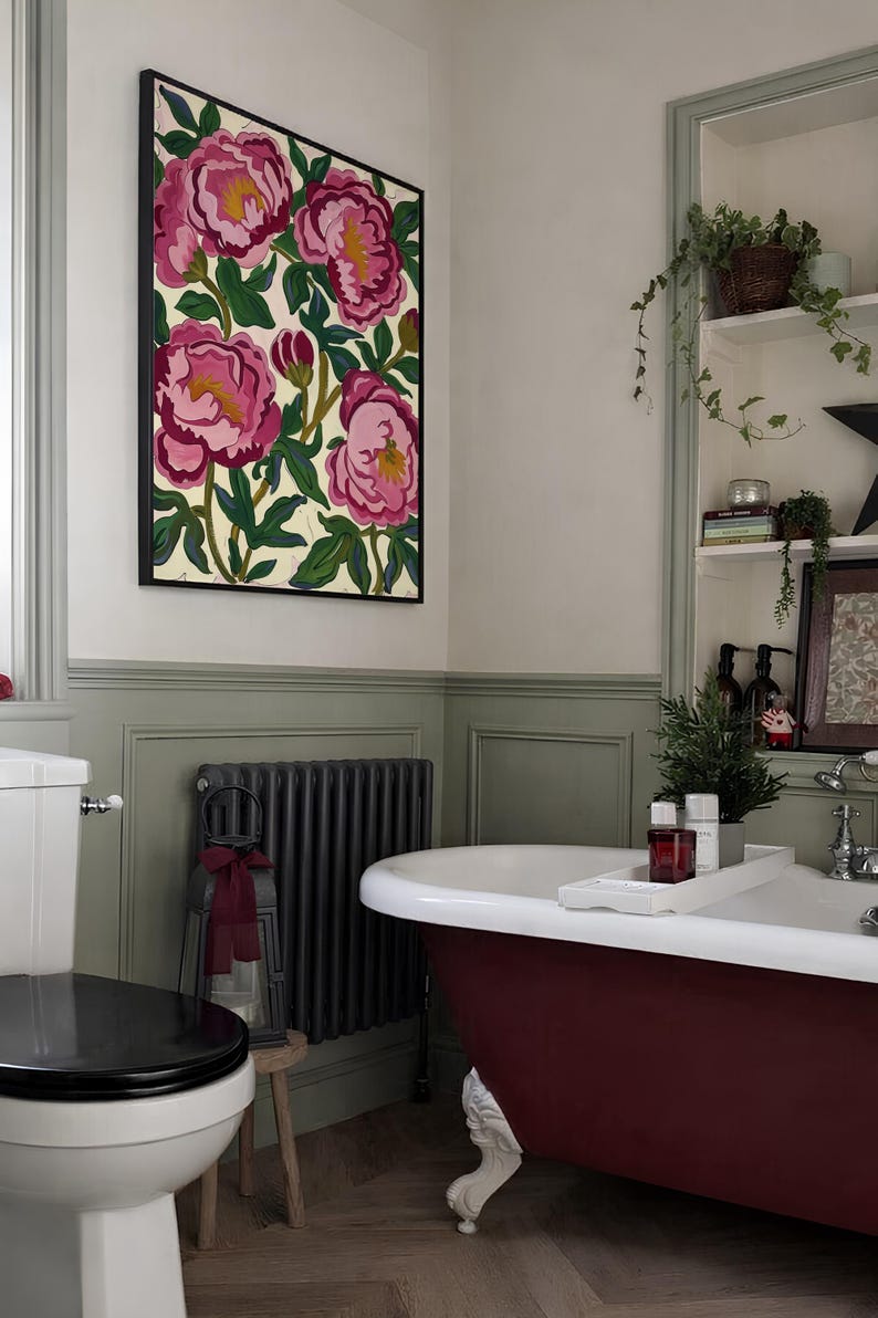 May include: A bathroom scene featuring a framed floral artwork with pink peonies. A burgundy clawfoot bathtub is in the foreground, complemented by a black radiator and a white toilet. The walls are painted in neutral tones.