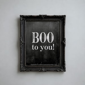 May include: A rectangular black ornate frame containing a dark chalkboard-style surface. The text "BOO to you!" is printed in white, stylized, serif lettering in the center of the frame, creating a high-contrast visual display.