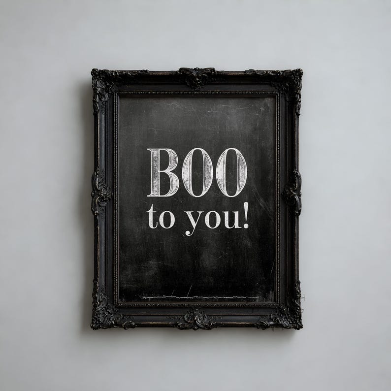 May include: A rectangular black ornate frame containing a dark chalkboard-style surface. The text "BOO to you!" is printed in white, stylized, serif lettering in the center of the frame, creating a high-contrast visual display.