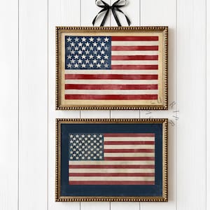 Può includere: Due stampe incorniciate della bandiera americana. La stampa superiore ha uno sfondo beige, mentre la stampa inferiore ha uno sfondo blu navy. Entrambe le bandiere presentano strisce rosse e bianche e un campo blu con stelle bianche. Le cornici sono dorate.