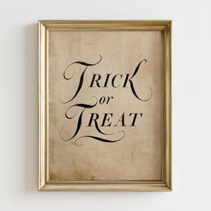 May include: A framed wall art piece featuring the black text Trick or Treat in a decorative, swirling script font. The background is a light tan, textured paper with a vintage, aged appearance. The frame is a metallic gold with a simple profile.