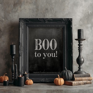 May include: A black ornate picture frame containing a chalkboard with the white text BOO to you! The frame is surrounded by black candlesticks, black candles, and small orange and black pumpkins resting on a stack of vintage books.