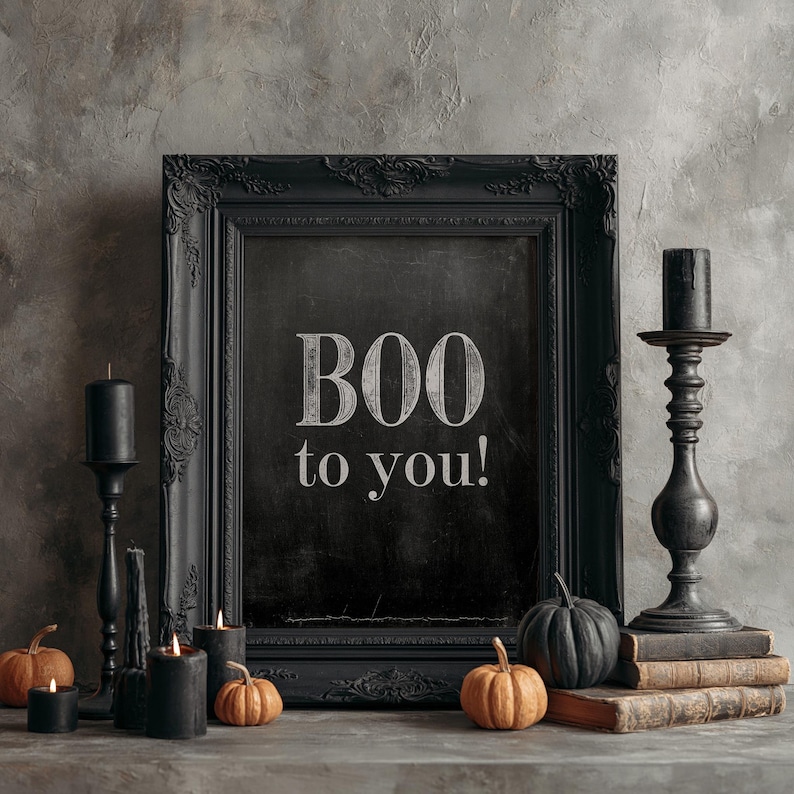 May include: A black ornate picture frame containing a chalkboard with the white text BOO to you! The frame is surrounded by black candlesticks, black candles, and small orange and black pumpkins resting on a stack of vintage books.