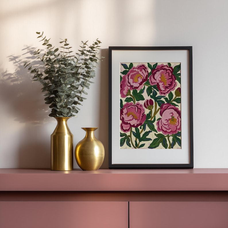 May include: A framed floral print featuring pink peonies with yellow centers and green leaves. Two gold vases and a vase of eucalyptus sit on a pink surface, creating a decorative display.