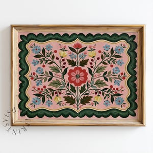 May include: A rectangular framed print featuring a symmetrical floral illustration on a light pink background. The design includes a central red flower, blue blossoms, yellow buds, and green leaves, all enclosed by a dark green scalloped border.