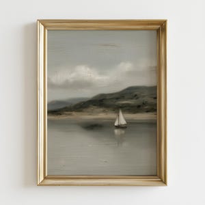 May include: A framed landscape painting featuring a sailboat on a calm lake. The artwork has a muted color palette with shades of gray, beige, and green. The gold frame adds a touch of elegance to the serene scene, depicting a cloudy sky and distant hills.