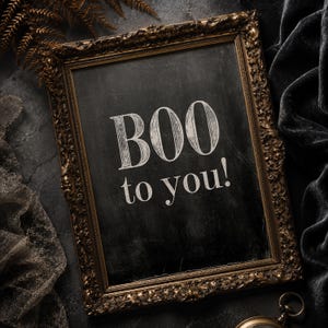 May include: A rectangular wall sign featuring an ornate, antique-style gold frame surrounding a black chalkboard surface. The text "BOO to you!" is printed in a white, serif font in the center of the board, with a distressed, weathered texture.