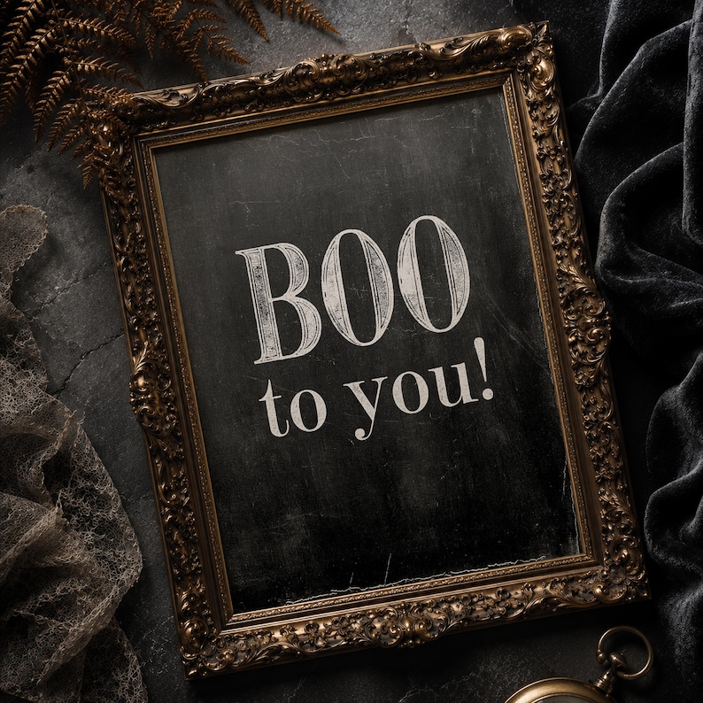 May include: A rectangular wall sign featuring an ornate, antique-style gold frame surrounding a black chalkboard surface. The text "BOO to you!" is printed in a white, serif font in the center of the board, with a distressed, weathered texture.
