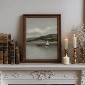May include: A framed landscape painting of a sailboat on a calm lake, with a mountain in the background. The painting is in a dark wooden frame and sits on a white mantelpiece, next to lit candles and antique books.