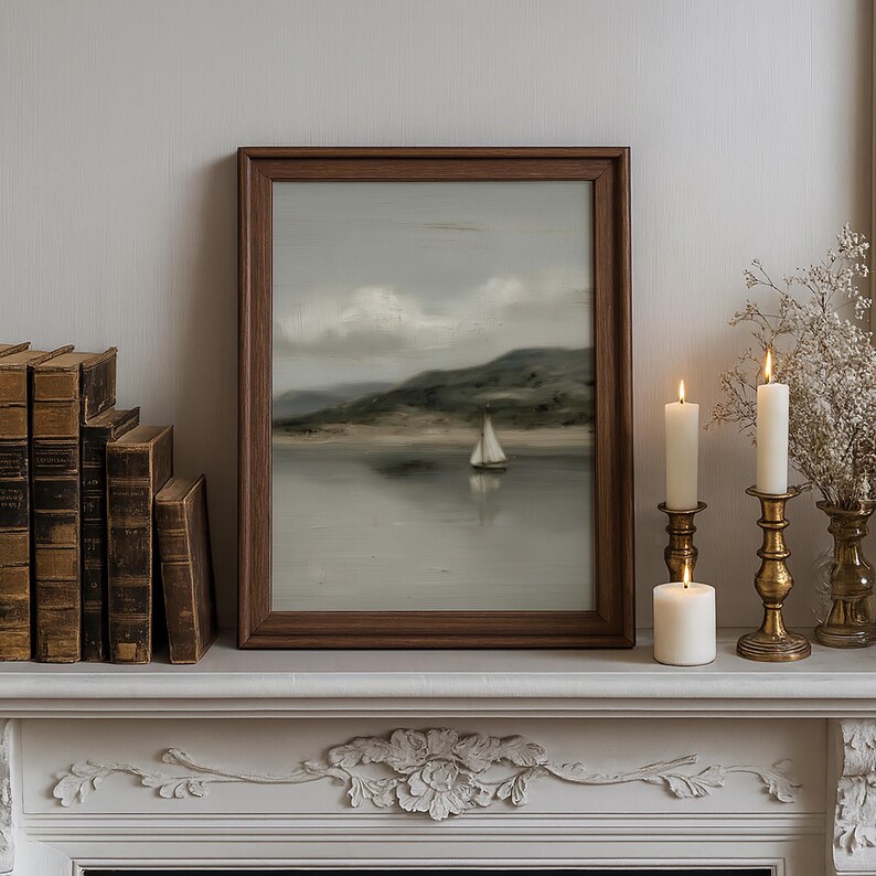 May include: A framed landscape painting of a sailboat on a calm lake, with a mountain in the background. The painting is in a dark wooden frame and sits on a white mantelpiece, next to lit candles and antique books.