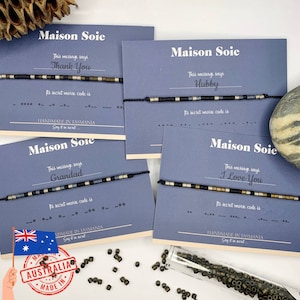 May include: Four cards with blue backgrounds and white text. Each card features a bracelet with black string and colourful beads. The cards say "Maison Soie" and include the message the bracelet represents in Morse code. The messages are "Thank You", "Hubby", "Grandad", and "I Love You".