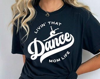 May include: Black t-shirt with white text that reads "Livin' That Dance Mom Life" with a silhouette of a dancer in the middle of the word "Dance".