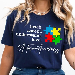 May include: A navy blue t-shirt with a white graphic of a jigsaw piece and the text "teach. accept. understand. love. Autism Awareness".