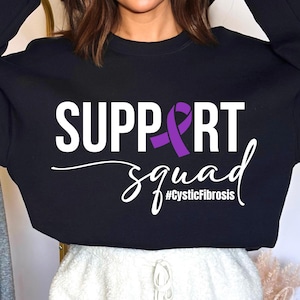 Puede incluir: Sudadera negra con texto blanco que dice "SUPPORT squad #CysticFibrosis" y una cinta morada.