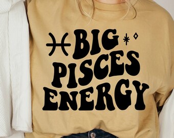 May include: A mustard yellow t-shirt with black text that reads "BIG PISCES ENERGY" and a Pisces astrological symbol.