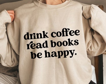 May include: A beige sweatshirt with the text "drink coffee read books be happy" in black. The sweatshirt is a neutral color and has a relaxed fit. The text is in a bold, sans-serif font.