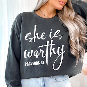 May include: A dark gray cropped sweatshirt with the text "she is worthy PROVERBS 31" in white.
