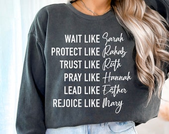 May include: A dark gray sweatshirt with white text that reads "WAIT LIKE Sarah PROTECT LIKE Rahab TRUST LIKE Ruth PRAY LIKE Hannah LEAD LIKE Esther REJOICE LIKE Mary"