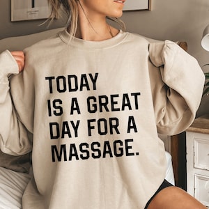 Op de afbeelding: Een beige sweatshirt met de tekst "TODAY IS A GREAT DAY FOR A MASSAGE." in zwart gedrukt.