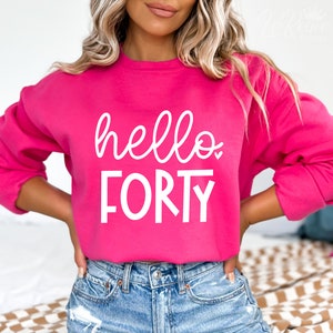 Puede incluir: Una sudadera rosa con el texto "hello forty" en letras blancas.