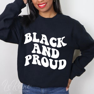 以下が含まれることがあります： レトロなフォントで「Black and Proud」と書かれた白いテキストが入った黒いスウェットシャツです。