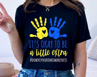 May include: Black t-shirt with yellow and blue handprints and the text "It's okay to be a little extra #downsyndromeawareness"
