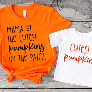 Könnte beinhalten: Zwei orangefarbene und weiße T-Shirts mit Halloween-Motiv. Das größere Shirt trägt den Schriftzug "Mama of the cutest pumpkins in the patch." Das kleinere Shirt trägt den Schriftzug "Cutest pumpkin."