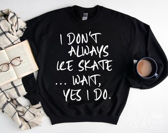 May include: Black sweatshirt with the text "I don't always ice skate... wait, yes I do" in white. The sweatshirt is paired with a book, glasses, a scarf, and a mug of coffee.