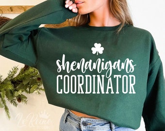 May include: A dark green sweatshirt with white text that reads "Shenanigans Coordinator" and a small shamrock graphic.