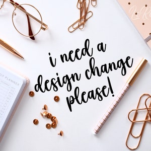 Peut inclure: Un fond blanc avec le texte "i need a design change please!" écrit en cursive noire. Il y a des trombones dorés, des punaises, un stylo rose avec des accents dorés, un stylo doré, une paire de lunettes et un agenda rose avec le texte "YEARLY PLANNER" sur la couverture.