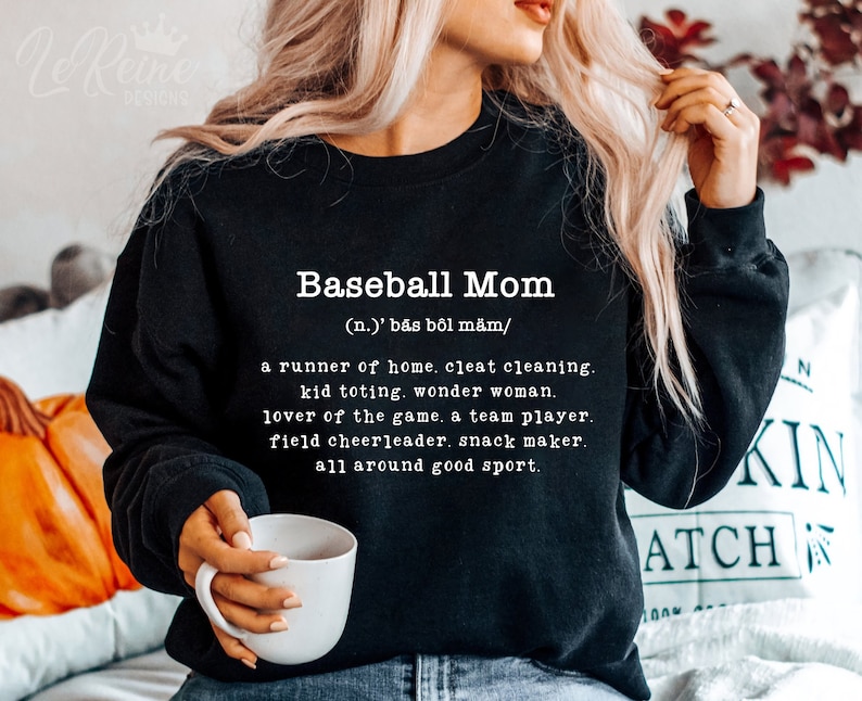 May include: Black sweatshirt with white text that reads "Baseball Mom (n.) 'bās b&ocirc;l m&auml;m/ a runner of home. cleat cleaning. kid toting. wonder woman. lover of the game. a team player. field cheerleader. snack maker. all around good sport."