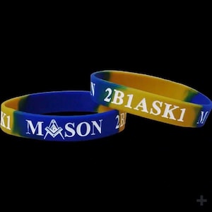 May include: Two blue and yellow silicone wristbands. One band reads "MASON" with a Masonic symbol, the other reads "2B1ASK1" in white letters. The bands are on a black background.