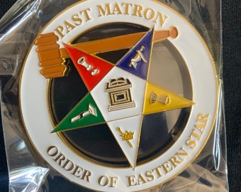 May include: A white and gold circular car emblem with the text "Past Matron Order of Eastern Star". The emblem features a five-pointed star with a gold border and a black center. The star is divided into five sections, each with a different color and symbol.