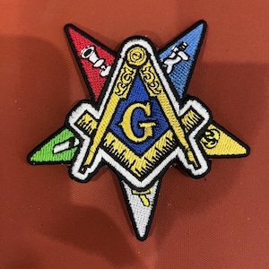 May include: Embroidered patch featuring a Masonic symbol, a compass and square with a letter "G" in the center. The patch is in a star shape with red, blue, green, yellow, and white accents. The patch is on a reddish-brown surface.
