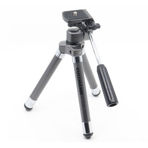 Op de afbeelding: Een grijs, compact statief met een zwarte handgreep en een zwarte snelkoppelingsplaat. Het statief is gemarkeerd met "Cullmann".