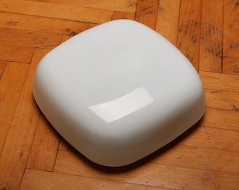 May include: A white ceramic bowl with a square shape and a smooth, glossy finish. The bowl is sitting on a wooden surface.