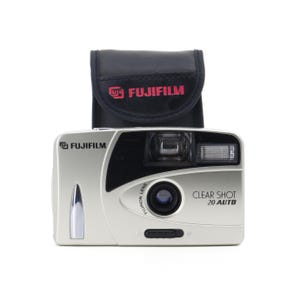 Puede incluir: Una cámara compacta Fujifilm Clear Shot 20 Auto plateada con una funda de cuero negra. La cámara tiene una lente Fujinon y un flash.
