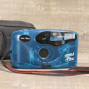 Könnte beinhalten: Eine blaue und schwarze Kompaktkamera mit einem roten Knopf und dem Text "Auto Flash", "CDS DX", "Red Eyes", "Formel 1" und "F3.5 Lens Auto Flash".