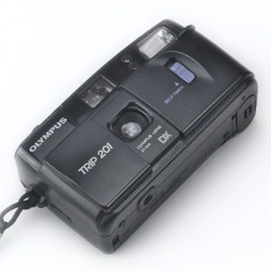 May include: A black Olympus Trip 201 point-and-shoot film camera with a self-timer and a 31mm Zuiko lens. The camera has a black strap attached.