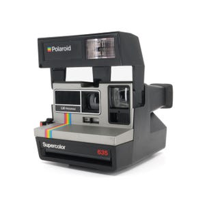 May include: A silver and black Polaroid 635 Supercolor instant camera with a built-in flash. The camera has a rainbow stripe design and the text "LM Program" on the front.