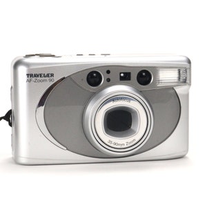 Op de afbeelding: Een zilverkleurige Traveler AF-Zoom 90 point-and-shoot camera met een 35-90mm zoomlens. De camera heeft een ingebouwde flitser en een autofocusfunctie.