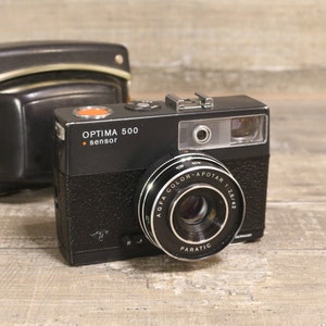 May include: A black Agfa Optima 500 sensor camera with a silver lens. The lens is labeled "Agfa Color-Apotar 1:2.8/42 Paratic".