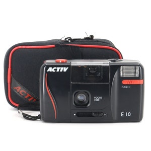 Op de afbeelding: Een zwarte en rode point-and-shoot camera met een ingebouwde flitser. De camera heeft het woord "ACTIV" in witte letters op de voorkant. De camera zit in een zwarte draagtas met een rode rits.