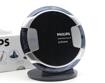 May include: A silver and black Philips 200 Seconds Magic ESP Expanium MP3 player with a circular design. The player is on a black stand.