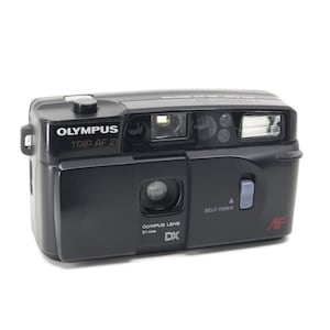 Op de afbeelding: Een zwarte Olympus Trip AF 21 point-and-shoot camera met een 31 mm DX lens. De camera heeft een zelfontspanner en een autofocusfunctie.