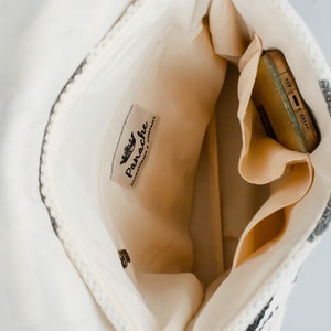 May include: Inside view of a white and black striped woven bag with a zipped pocket and a label that reads "Panache Accessories & Company."