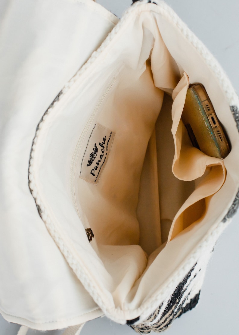 May include: Inside view of a white and black striped woven bag with a zipped pocket and a label that reads "Panache Accessories & Company."
