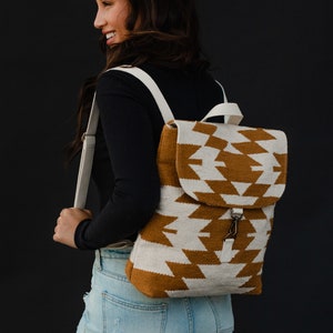 May include: A brown and white geometric patterned backpack with a white strap. The backpack has a flap with a buckle closure.